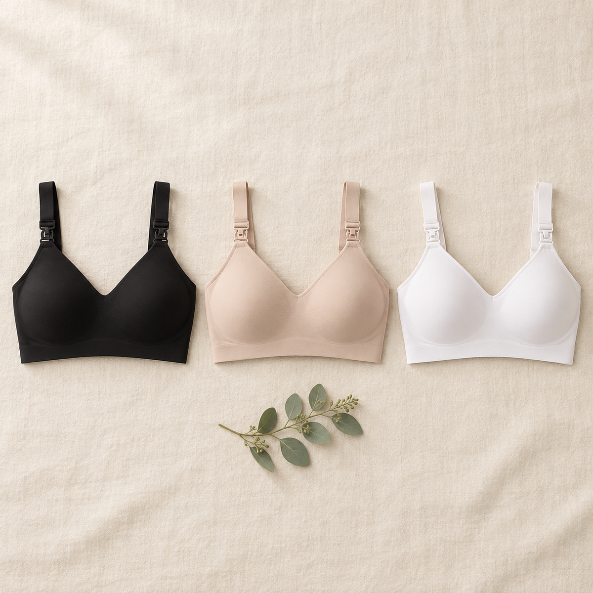 Three CloudSoft wire-free maternity and nursing bras in black, nude and white on a cream linen background.